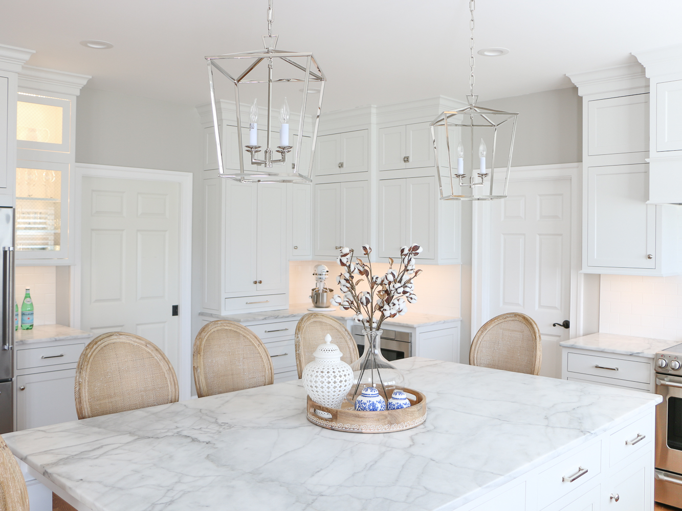 All white kitchen remodel with inset cabinets, carrara marble island, polished nickel pendants, cane back counter stools