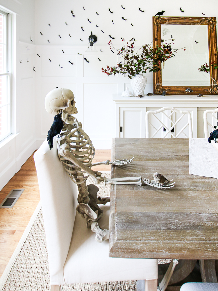black and white halloween decor including a skeleton, black bats, blackbirds in a white dining rom