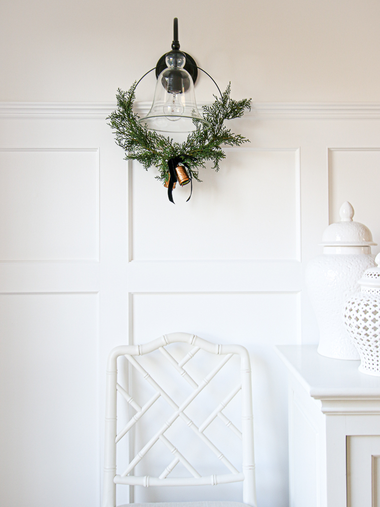 White dining room wall with wreath hung on black scones, white decor on white server, white dining chair