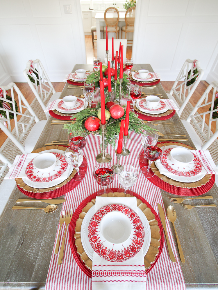 Christmas tablescape with traditional red color scheme in white dining room, elegant table settings, white dining chairs with boxwood wreaths on the back, red tapered candles, Christmas greenery centerpieces