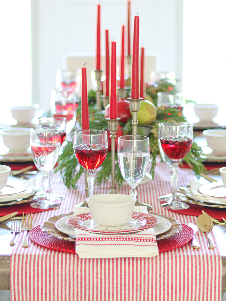 Elegant traditional  red Christmas tablescape with green and gold accents, tapered candles, crystal glasses, centerpieces with Christmas greenery and fruit, gold flatware