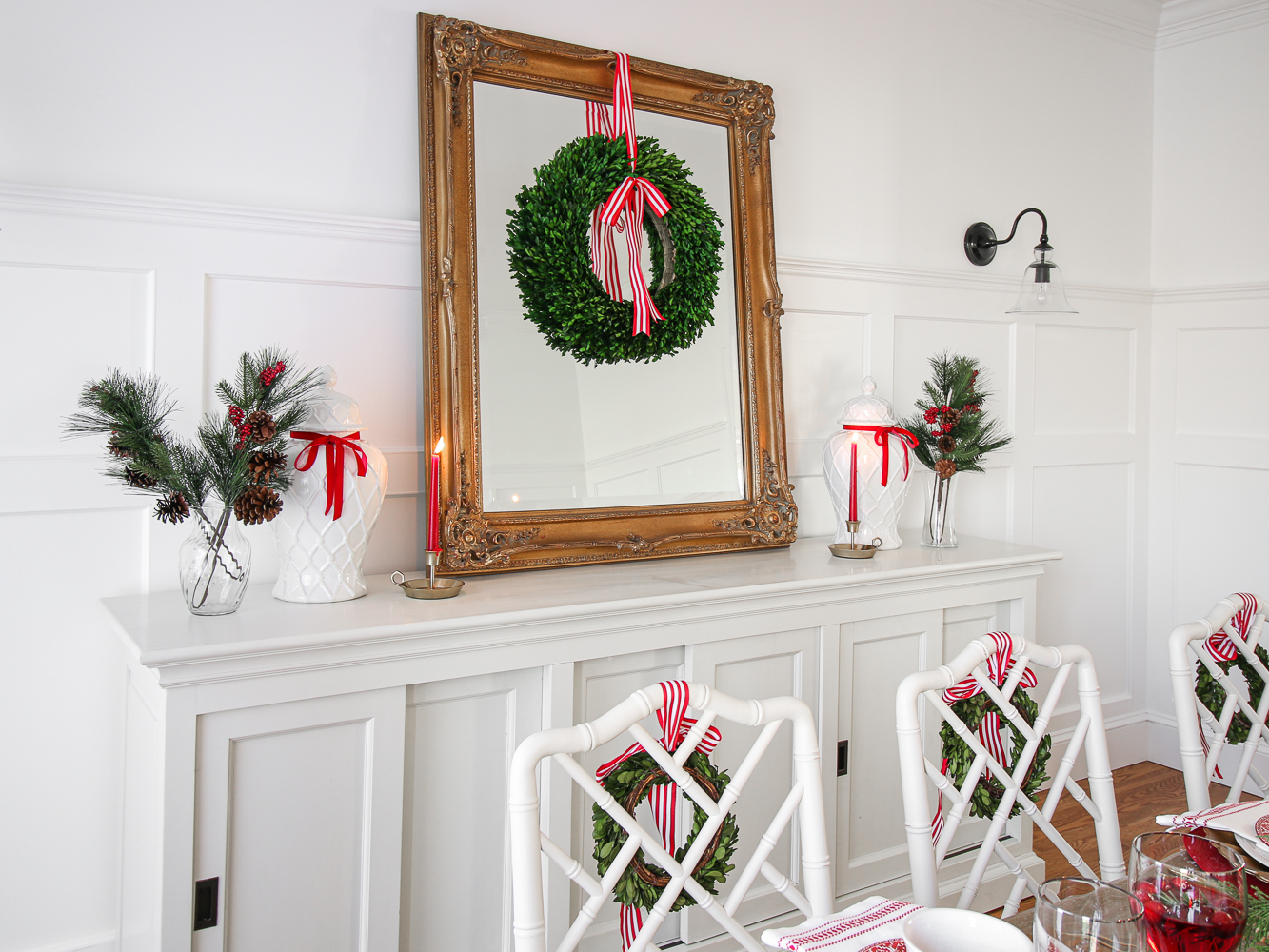 hang wreaths on mirrors, vintage gold mirror styled with boxwood wreath with decorative red and white striped bow, white dining room with wall molding, white sideboard, white chippendale chairs