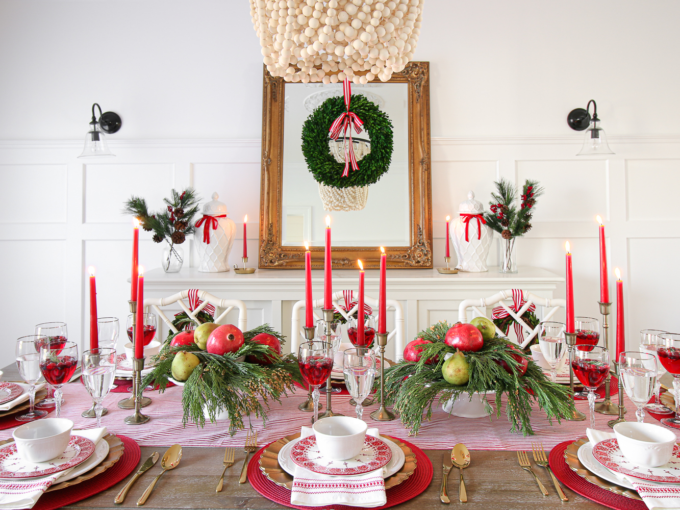 Christmas tablescape, antique mirror, wood bead chandelier, red ribbon, boxwood wreath, red candles, gold flatware, red and white table decor, Christmas greenery