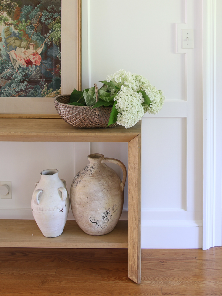 console table, artisan vases, needlepoint art girl on a swing, hydrangea bouquet in woven basket