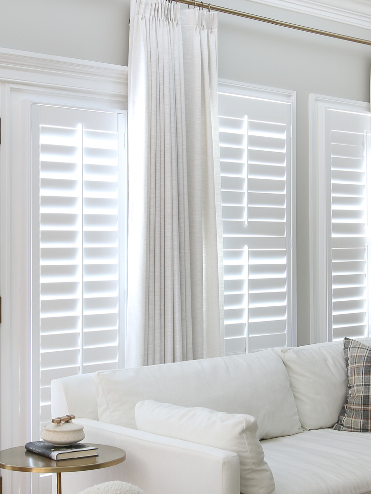 Interior window shutters, white velvet West Elm sofa, round metal side table, white linen pinch pleat drapes