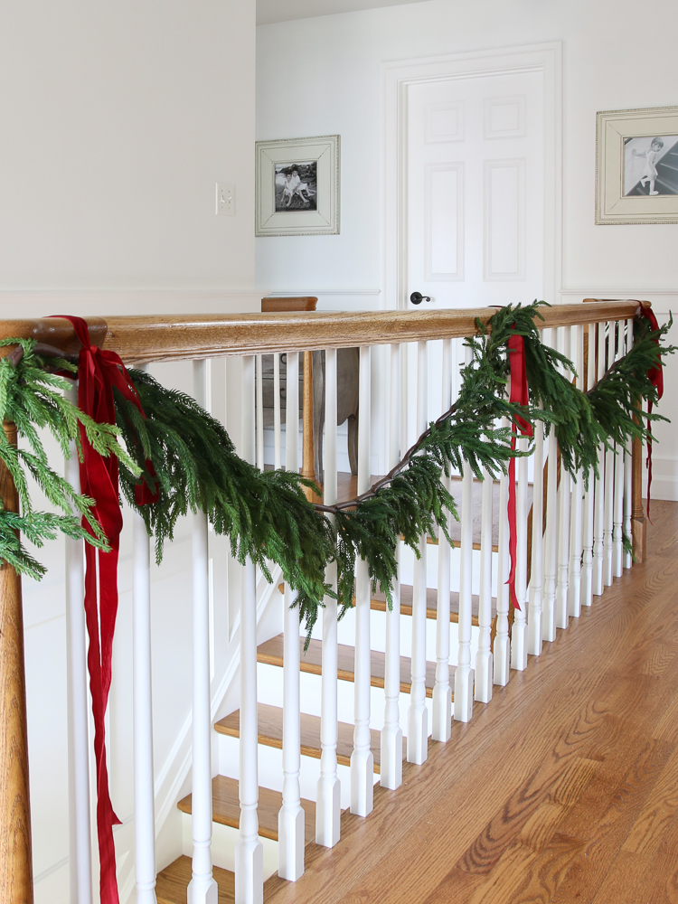 Best Christmas garland on the staircase landing banister, realistic garland Norfolk pine, red ribbon 