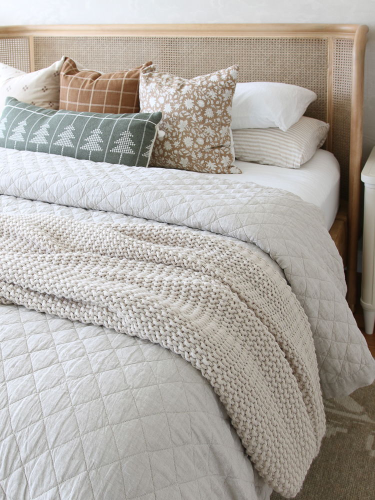 Fluffy bed styled with quilt, decorative throw pillows, chunky knit throw blanket