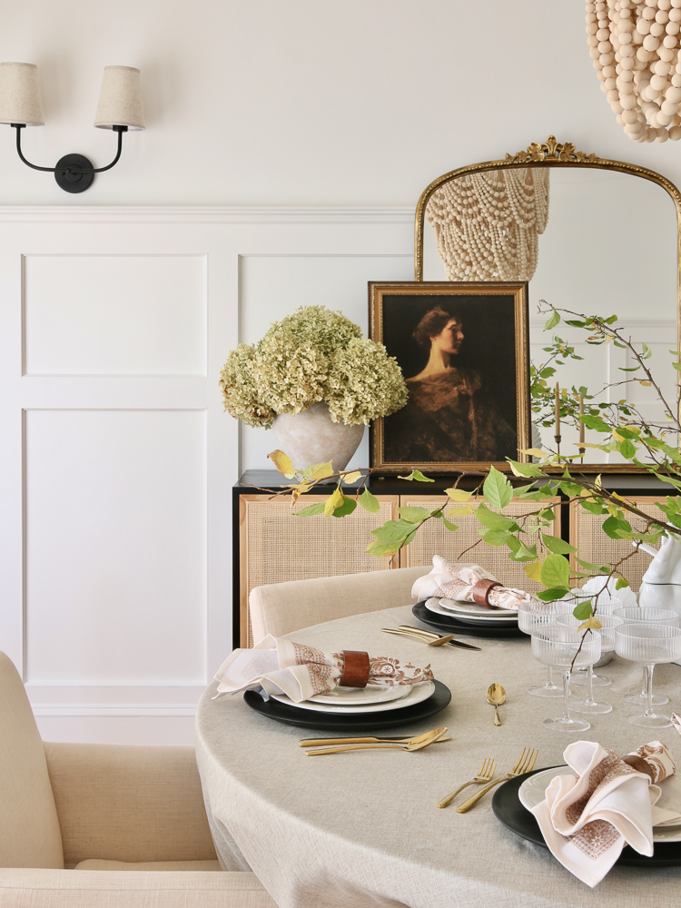 easy Thanksgiving table setting for round table, upholstered dining chairs, anthro gleaming primrose mirror, vintage art, wall molding, gold utensils, white everyday dinnerware, wood bead chandelier