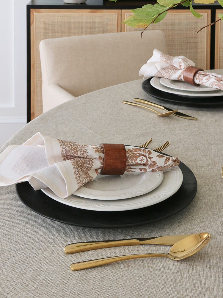 Round table setting, Thanksgiving table scape, round dining table with beige linen tablecloth, white everyday dishes, printed fall cloth napkins, gold utensils
