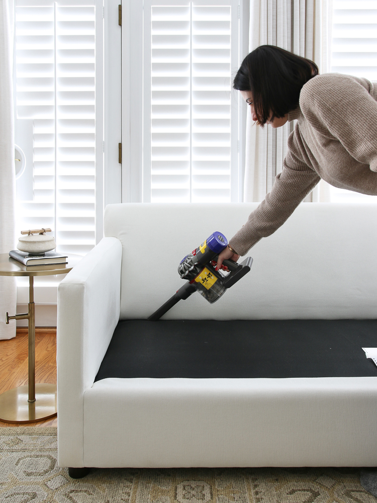 Person vacuuming under sofa cushions with crevice tool to clean fabric sofa