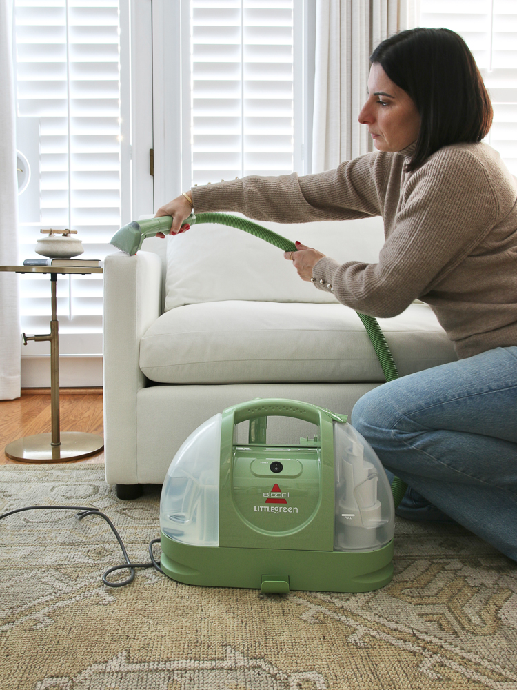 person demonstrating how to clean a fabric sofa with bissell little green machine
