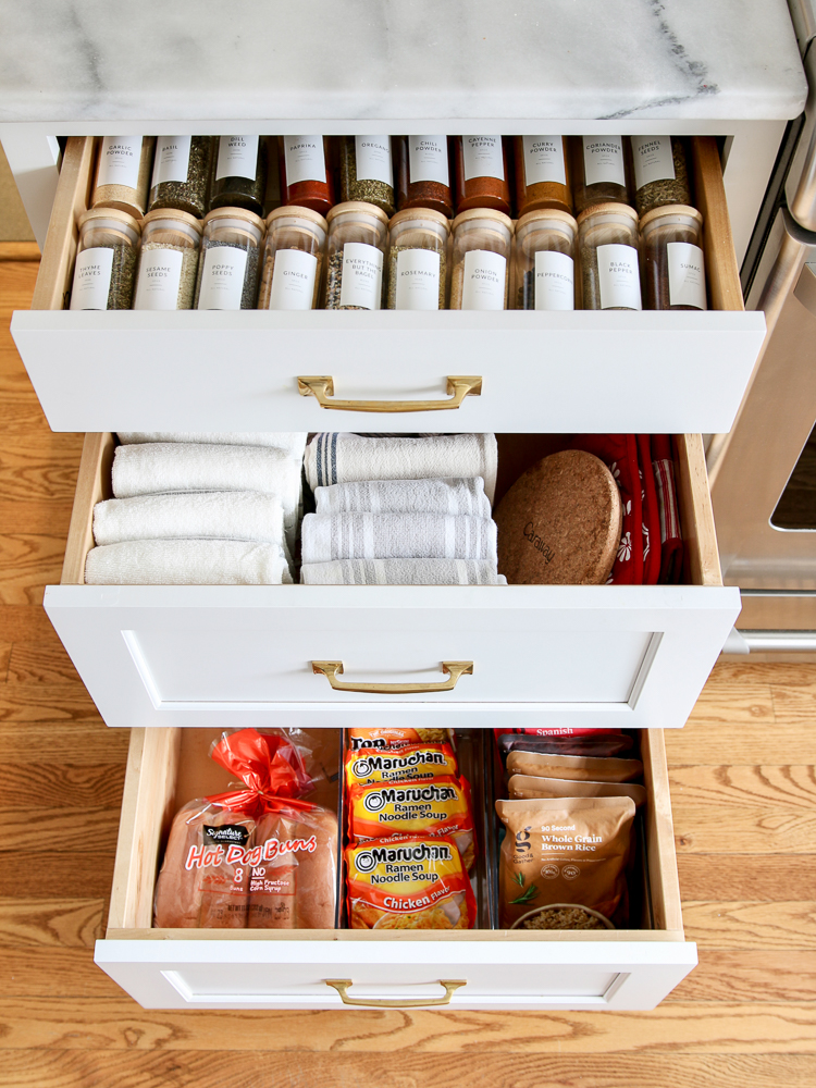 overhead view of 3 open drawers, top drawer has organized spices, middle drawer has organized kitchen linens, bottom drawer has organized bread and pasta, pantry cabinet and drawer storage