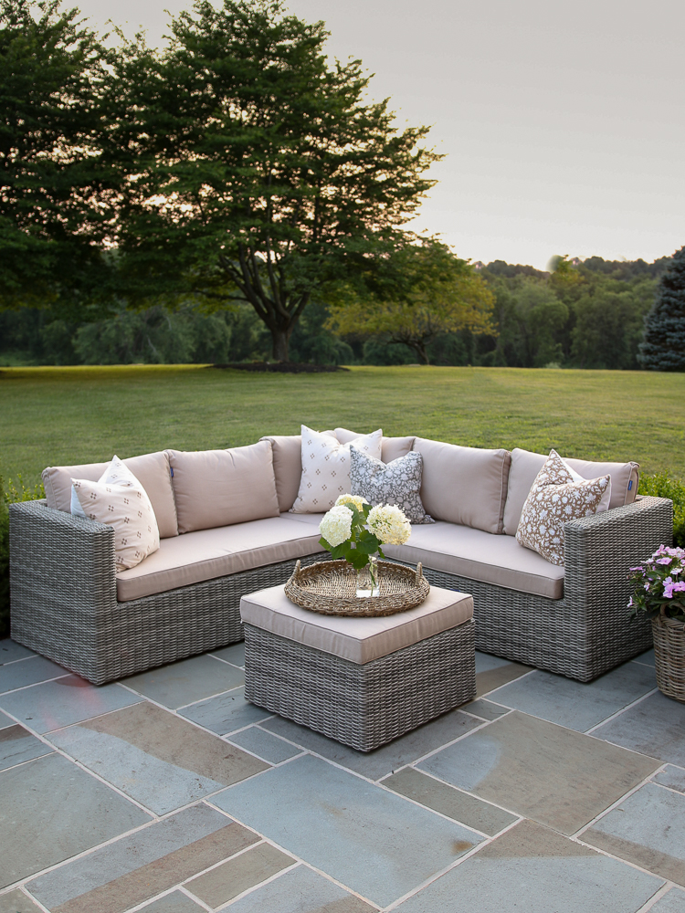 backyard view of bluestone patio and with wicker furniture, flowers, and manicured lawn 