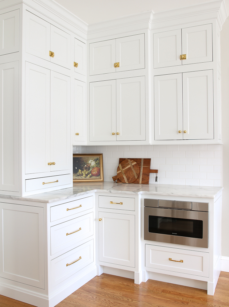 corner of white kitchen with brass cabinet hardware, wood floors, marble countertops