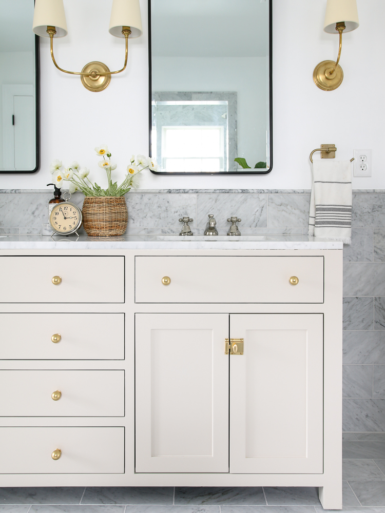 marble bathroom, accessible beige painted vanity with aged brass cabinet hardware, black medicine cabinet, brass sconces