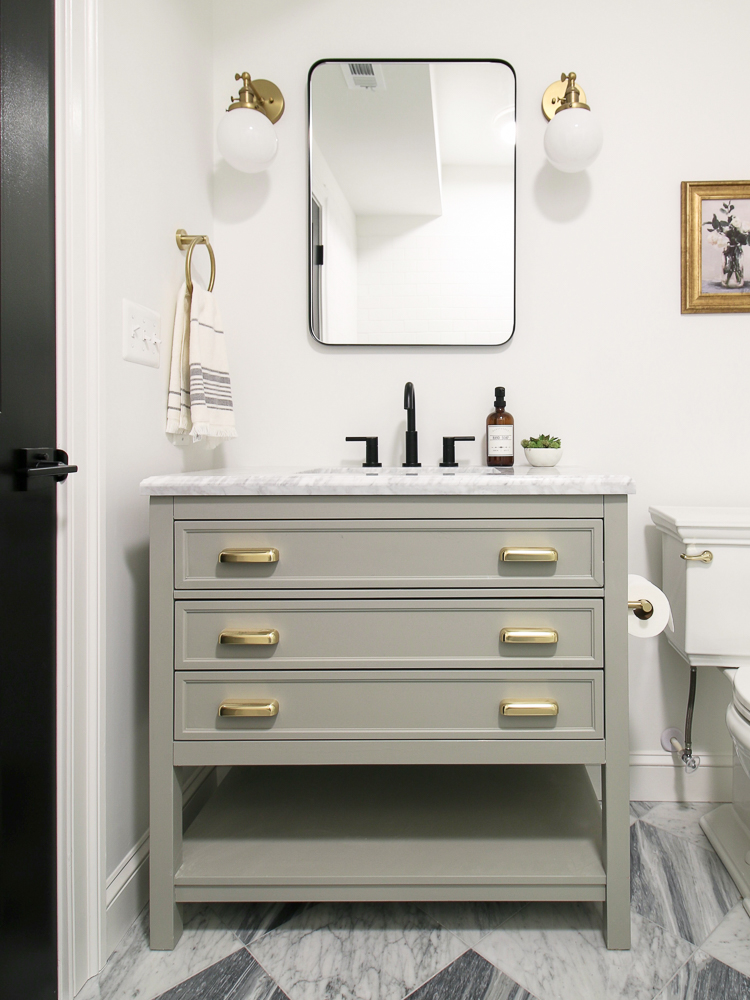 bathroom vanity with brass cabinet hardware, black faucet, medicine cabinet and brass sconces