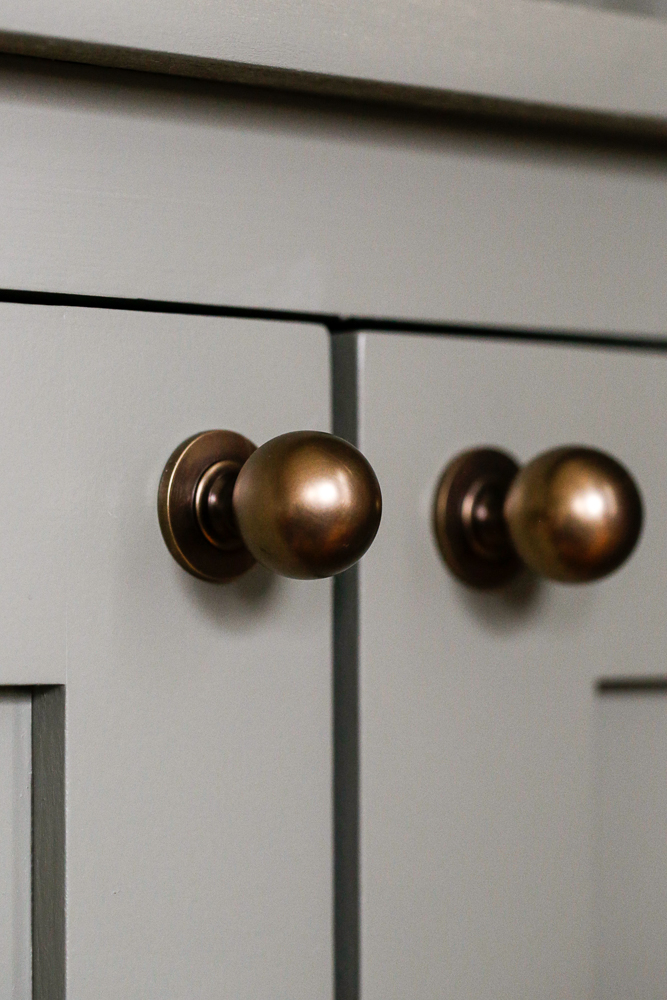 close up of round antique brass cabinet knobs on doors painted storm cloud gray