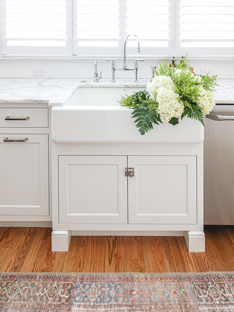 classic white kitchen, marble countertops, polished nickel hardware, white sink with fresh cut flowers