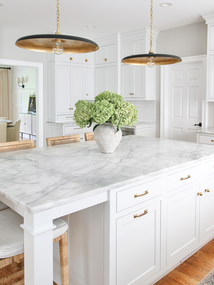 classic white kitchen with Carrara Marble countertops, brass hardware, and modern black and brass pendants