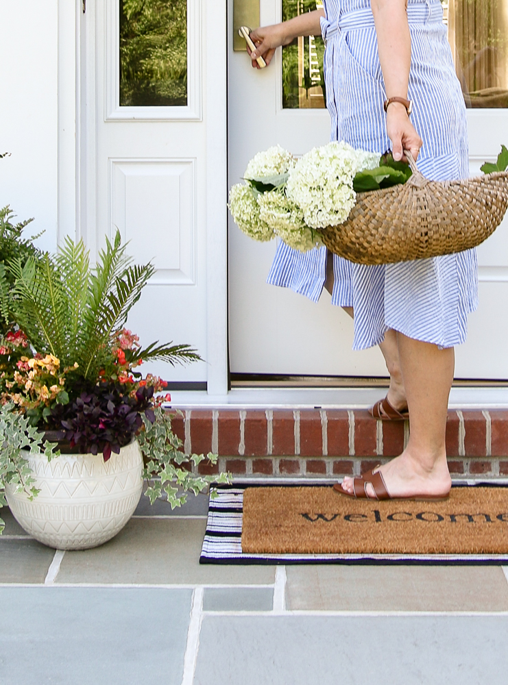 person approaching front door with basket of hydrangeas in hand