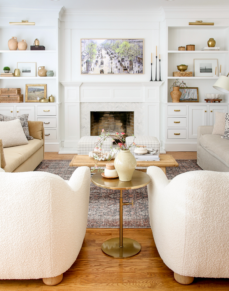 living room with updated white fireplace surround and building bookshelves, boucle chairs, velvet sofa, shelf decor