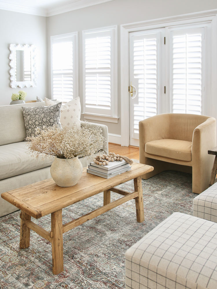 living room with white interior shutters, wood floors, linen sofa, velvet chair, and wooden coffee table