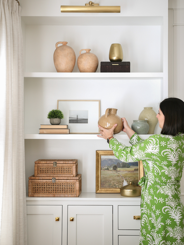 person demonstrating how to style shelves, placing vase on shelf