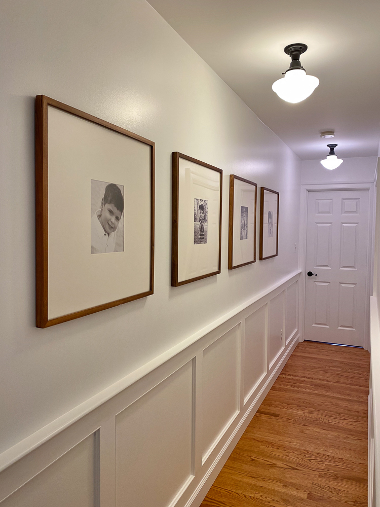 upstairs hallway with molding painted white with photos on wall and ceiling lights on
