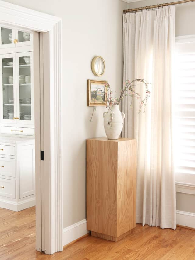 loving room corner with agreeable gray paint, wood pedestal with vase and stems in front of wall