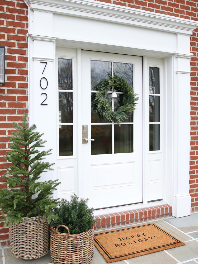 bluestone porch and white front door styled for holidays with faux wreath, shrubs, and tree