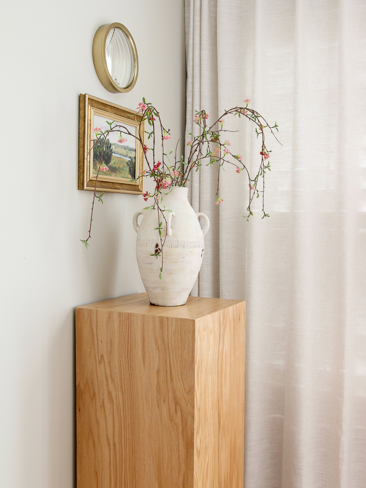 faux drooping stems and flowers in face on top of wooden pedestal