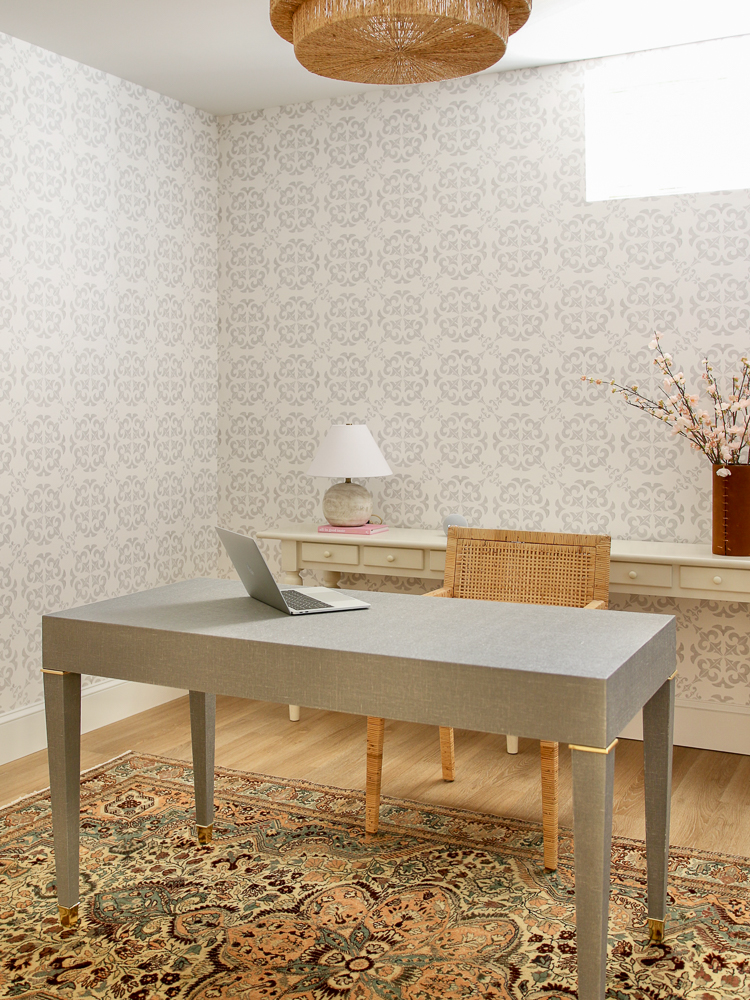 basement office with wallpaper that imitates tile work in gray and white, woven chandelier, gray desk, woven chair