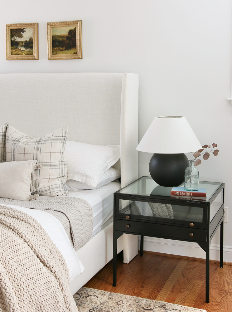 bedroom with white walls, white upholstered bed, black lamp and nightstand