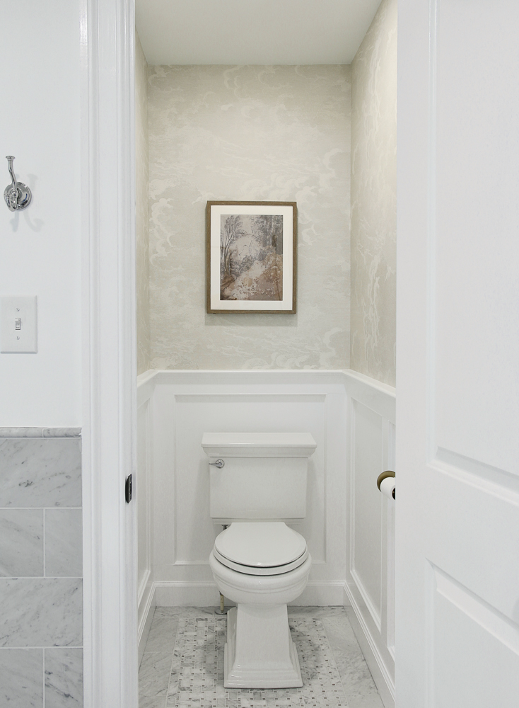 toilet room with door open showing novelette wallpaper on top part of walls, white wall molding on lower third of walls, marble tile flooring