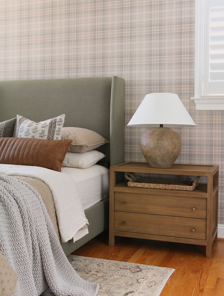 bedroom with check plaid wallpaper, gray upholstered bed, wooden nightstand, and brown lamp