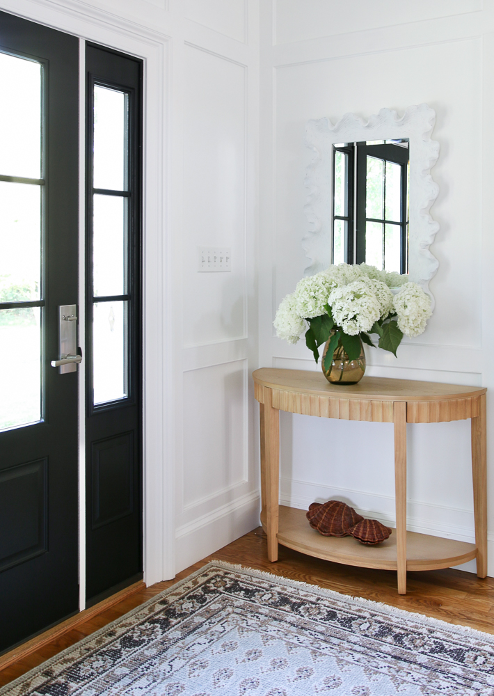 corner view of entry with black door, console table with vase a fresh cut hydrangeas