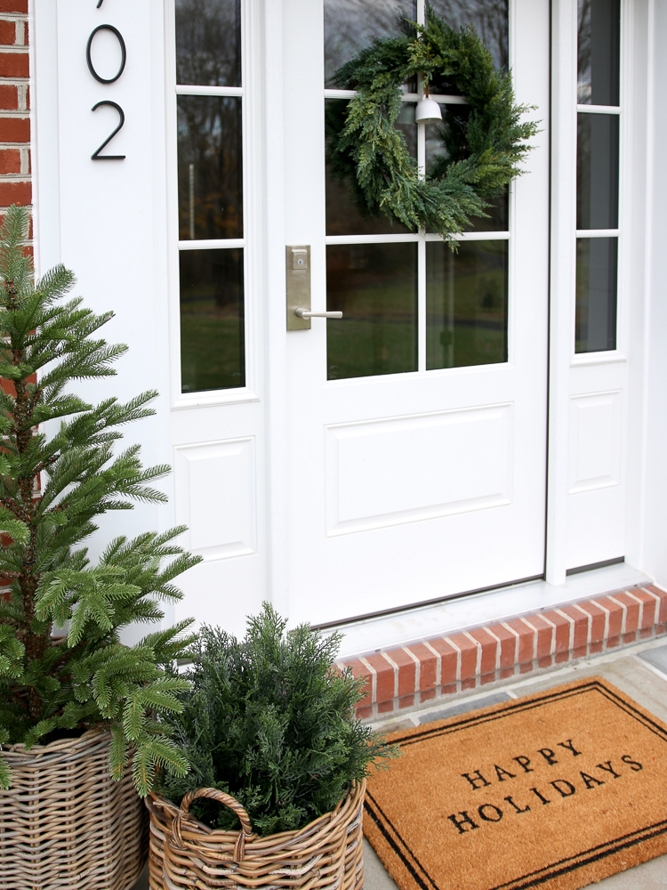 close up of front door with winter decor, artificial shrub, tree and wreath