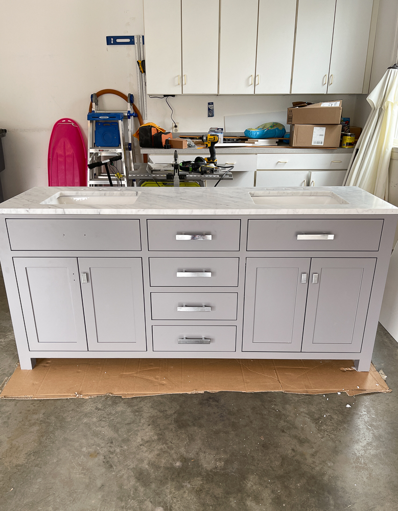 Factory vanity from Home Depot in a gray color, marble countertop and silver toned hardware. Vanity is in a garage and being prepped to paint. 