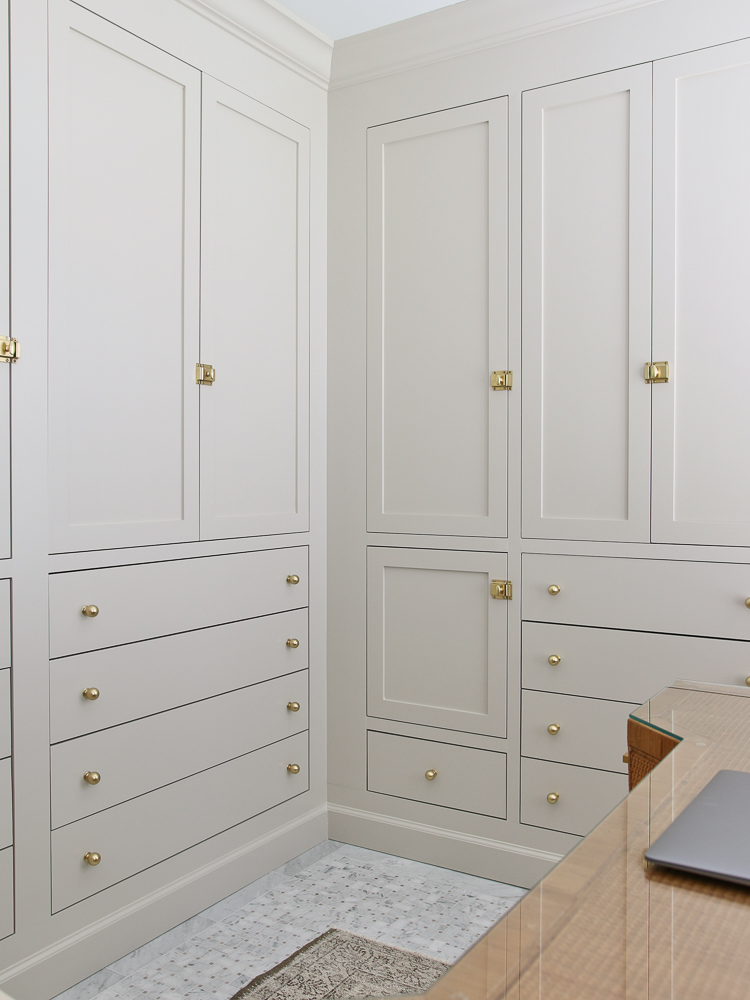 Opposite corner of primary closet with custom builtins painted Sherwin-Williams Accessible Beige and brass cabinet hardware. 