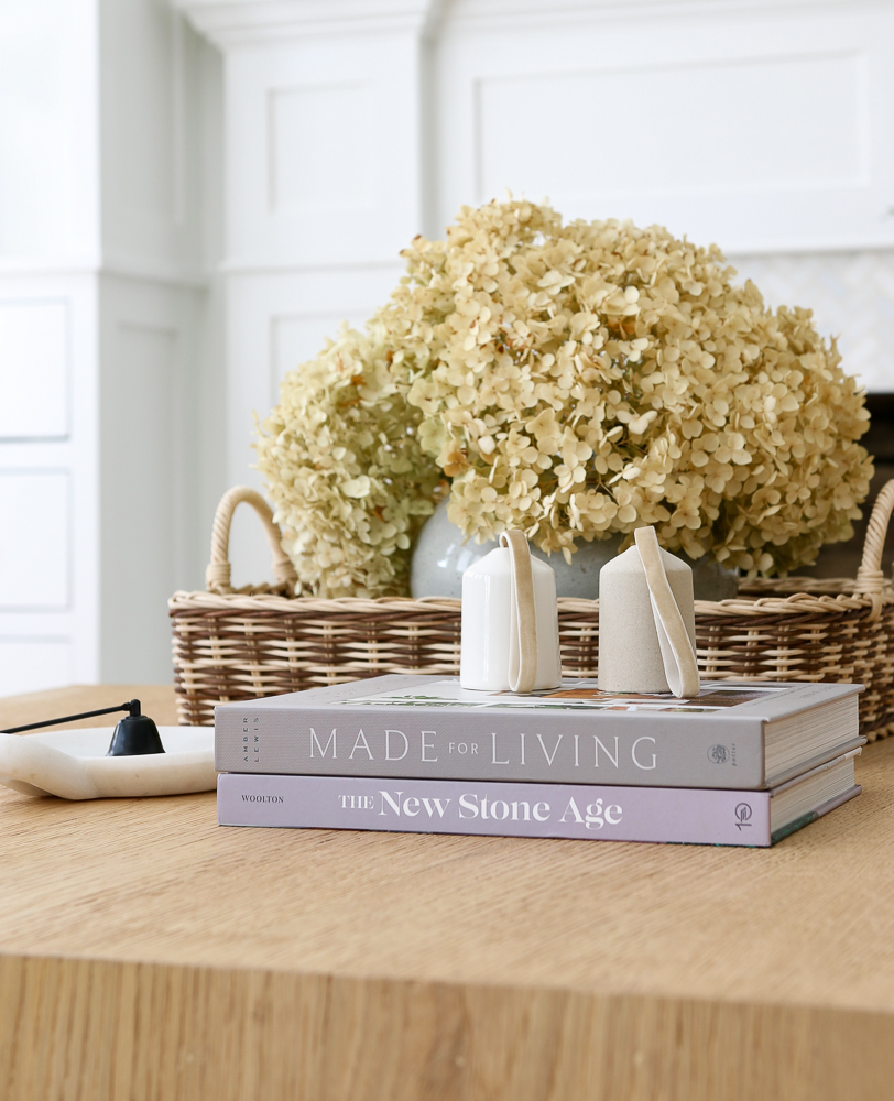 close up of decor to show decorating with coffee table books, stack of two books, candle snuffer, two-toned basket with dried hydrangeas