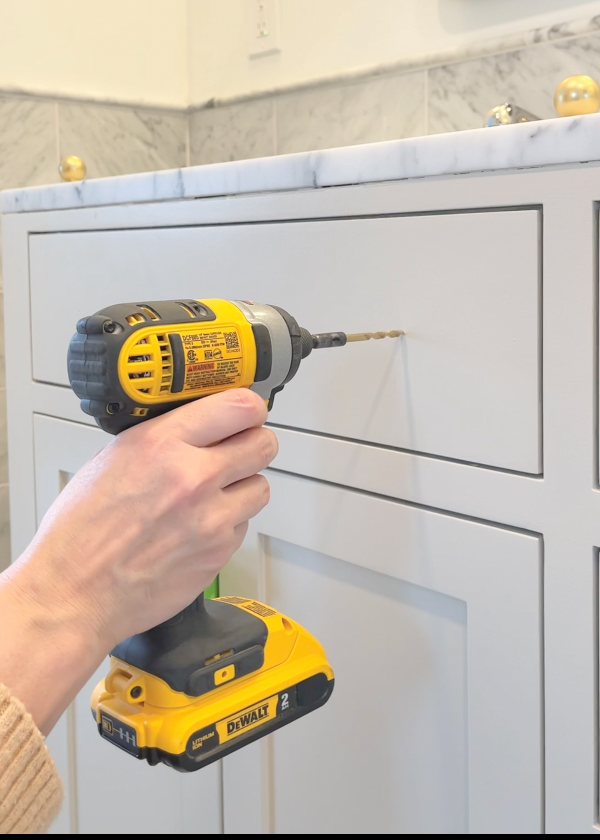 A drill being held to a bathroom cabinet to make a hole for hardware