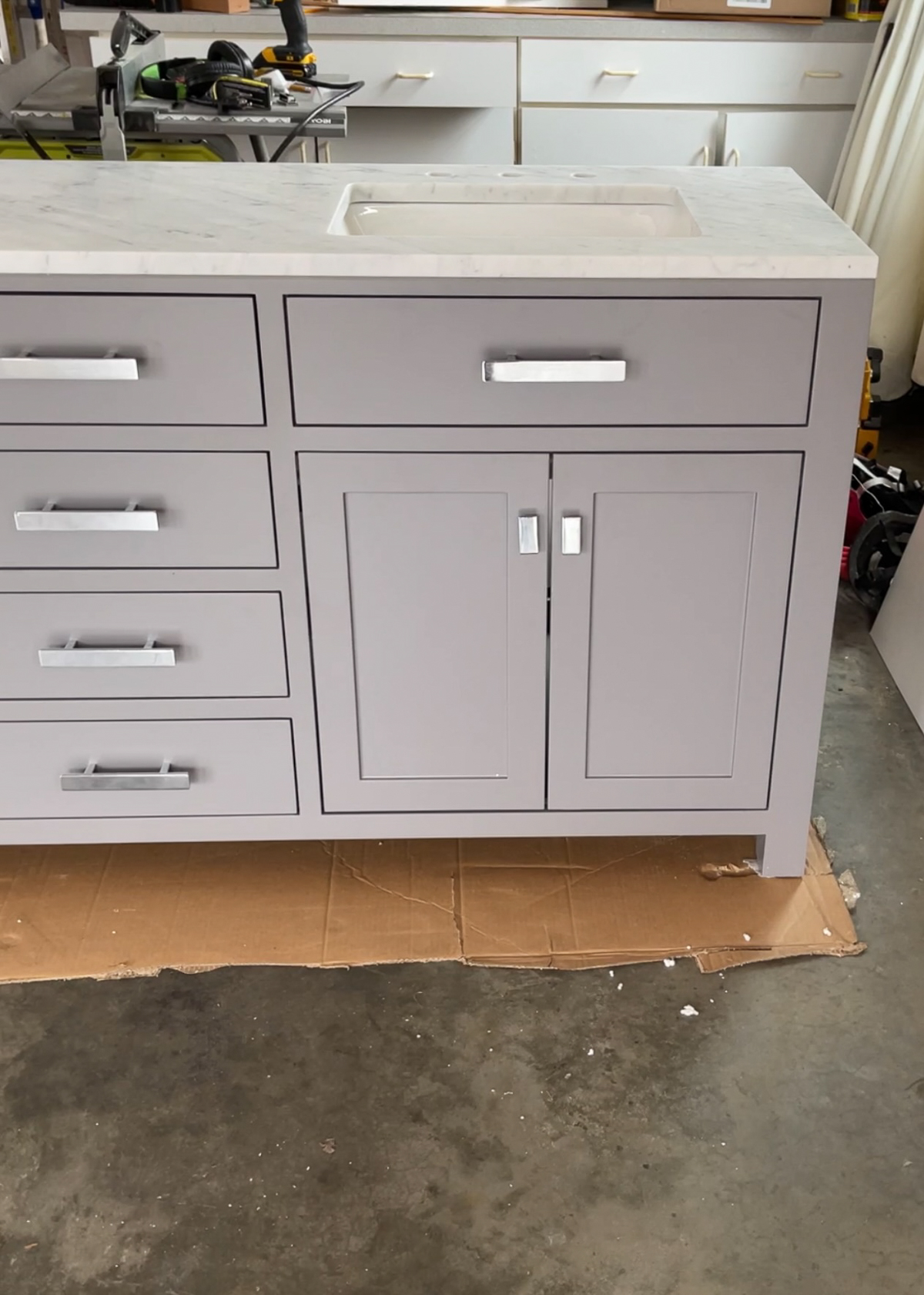 Grey bathroom vanity with chrome cabinet knobs and drawer pulls, marble countertop