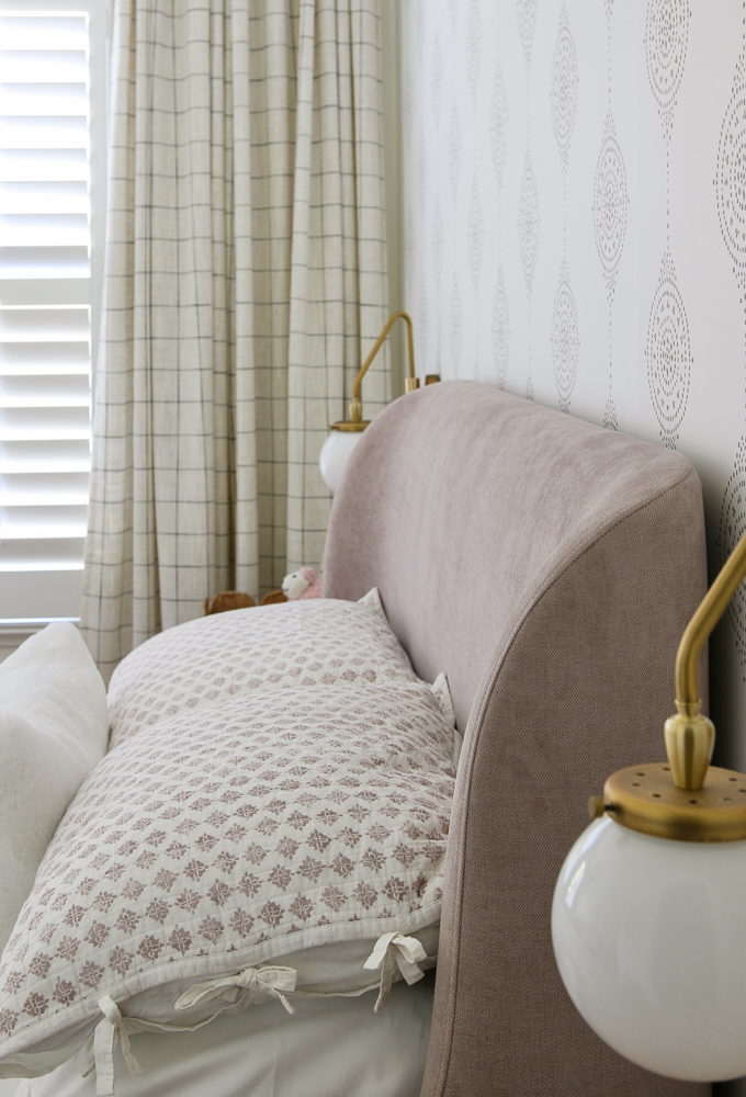 side view of mauve velvet headboard in girls room, brass sconces, Serena and Lily wallpaper, drapes and interior window shutters