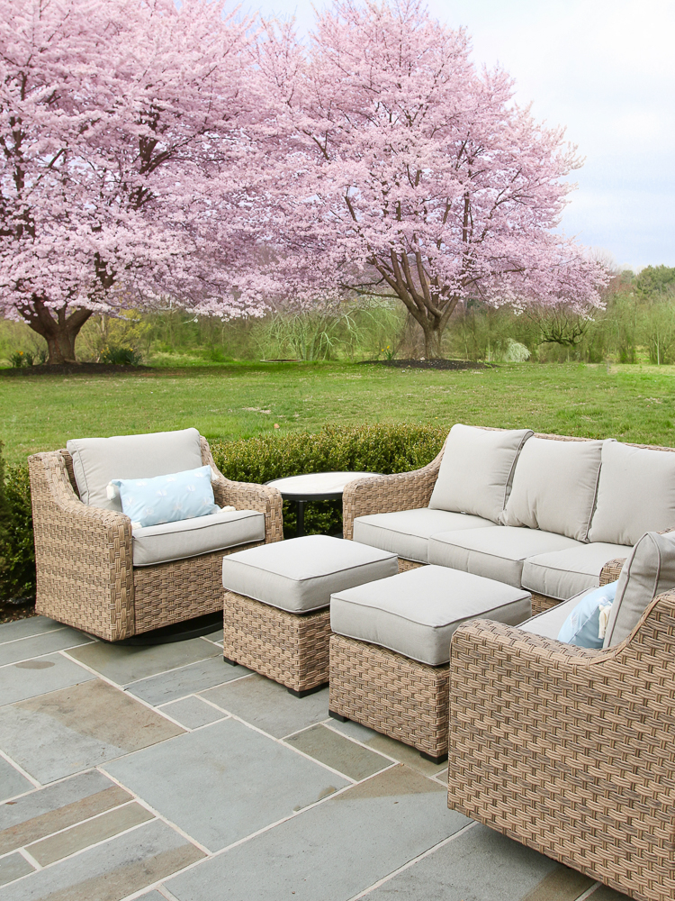 Outdoor wicker patio set, sofa, ottomans, and two chairs, pink cherry trees blooming in background