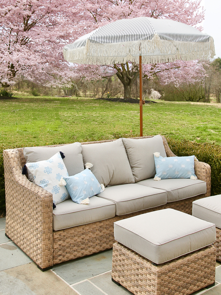 Outdoor wicker patio sofa and ottomans with blue throw pillows and striped fringe umbrella