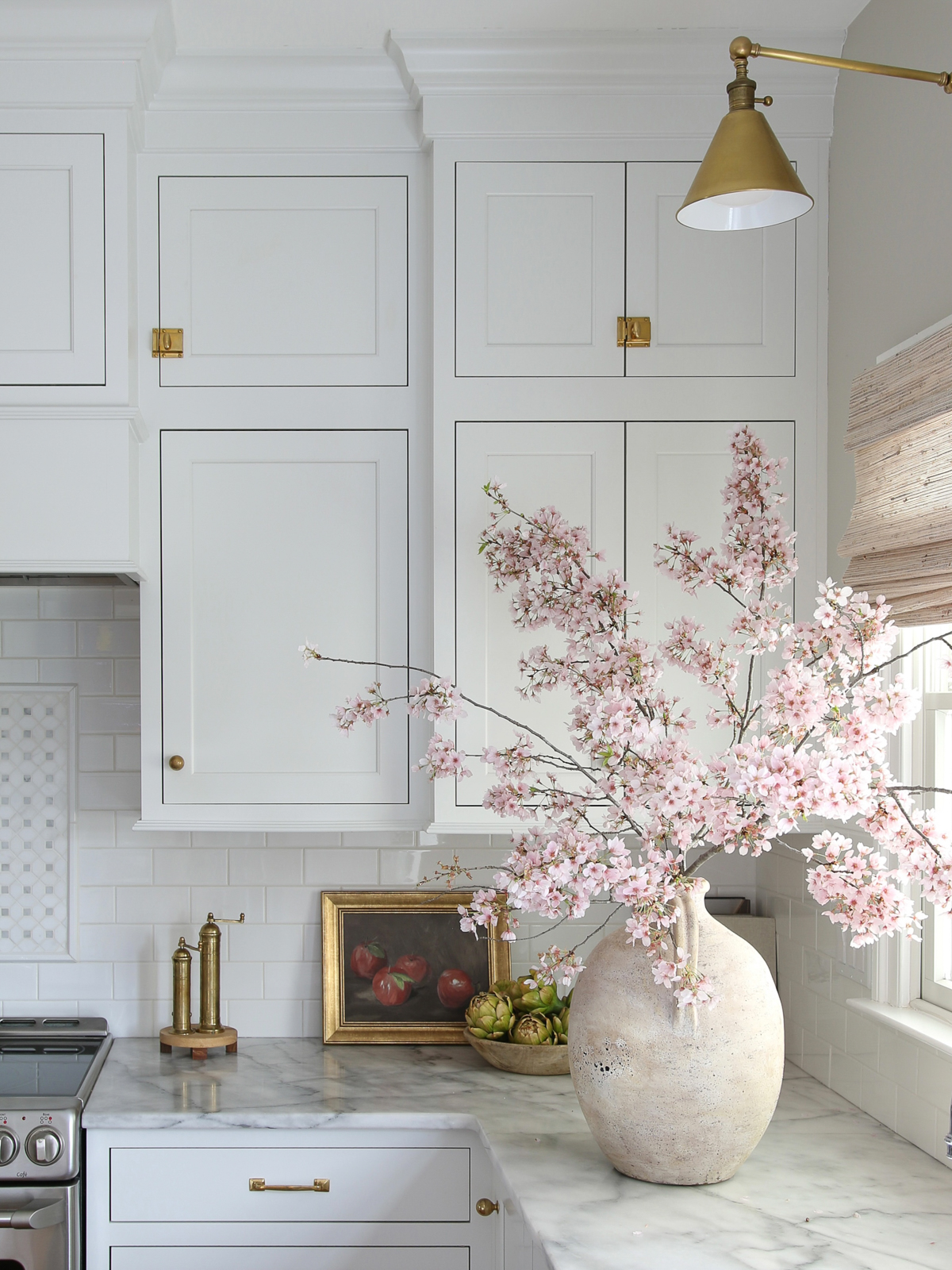 Large ceramic vase with cherry blossom branches on a marble countertop. White kitchen cabinets and white subway tile backsplash