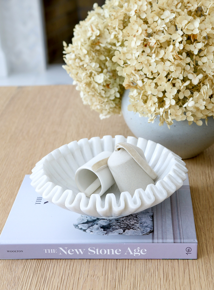close up of scalloped marble bowl styled on top of coffee table book, dried hydrangeas in vase