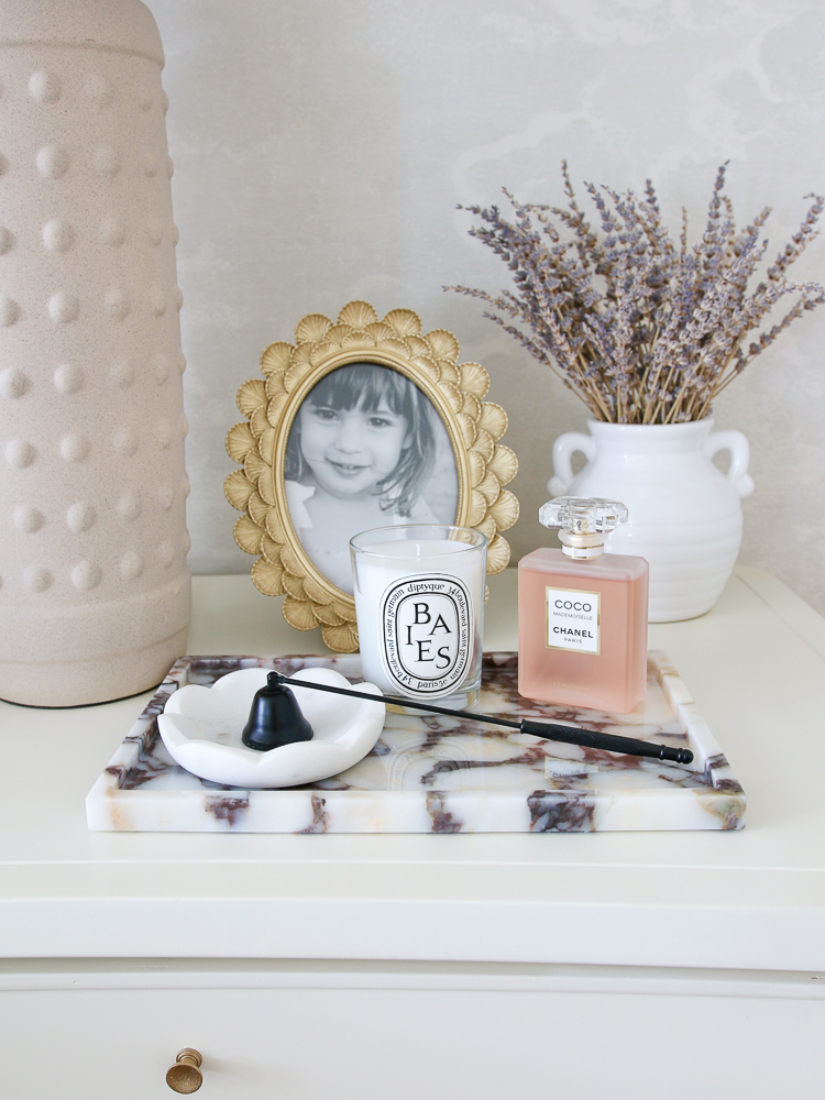 amazon home decor items styled on white nightstand with lamp, picture frame, marble tray, small scalloped marble dish, candle wick snuffer, candle, Chanel perfume