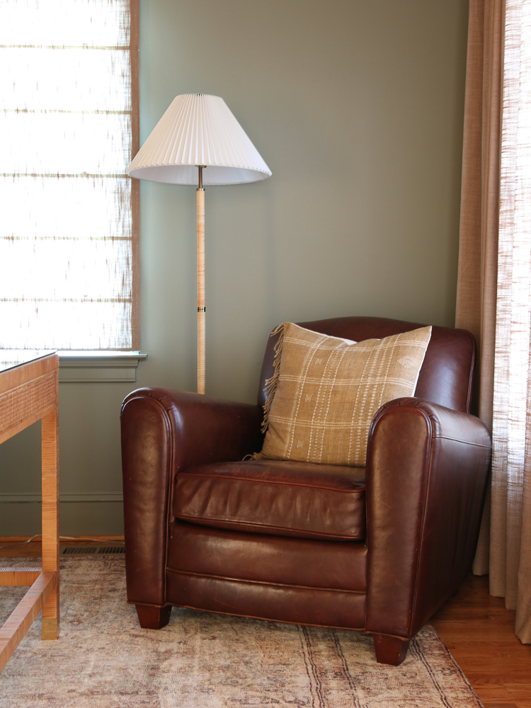 corner of room painted Storm Cloud Gray, leather armchair with throw pillow, lamp with pleated shaded, hardwood floors, Serena and lily desk, beige drapes
