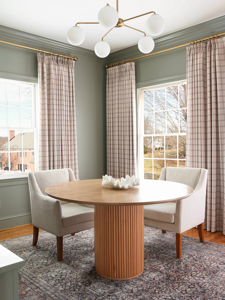 office space with Benjamin Moore storm cloud gray walls, Stefana Silber x Two pages drapes, round wood table with fluted base, light upholstered chairs, Loloii rug, brass and milk glass chandelier